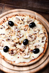 Pizza with champignons, black olives and mozzarella cheese. Wooden background. Soft focus.