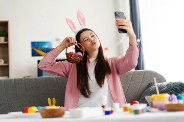Smiling beautiful teen girl taking selfie while holding easter eggs basket and making funny face