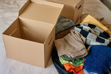 Open donation box with donated clothes on bed. Cardboard box with used clothes for recycling or...