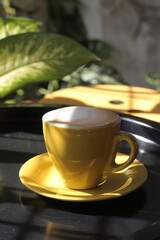 A cup of Cappuccino in yellow cup on the circle black table  