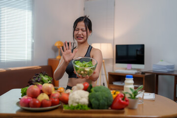 Young fitness woman refusing a bowl of salad with disgusted expression