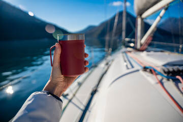 Woman hands holding thermo mug sitting on bow of the yacht during sailing in the morning in winter...