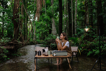 Fototapeta premium asain sitting on chair relax in stream drinking coffee in the morning, camping relax on vacation concept.