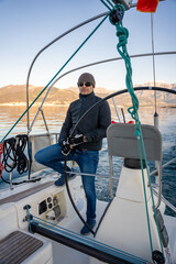 Young man captain standing at the helm and controls a sailboat during a journey by sea in winter time in Montenegro