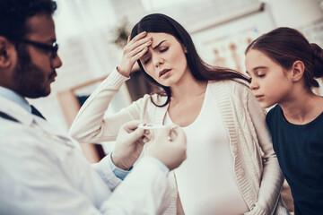 Indian doctor seeing patients in office. Doctor is listening to woman's symptoms. Woman has high...