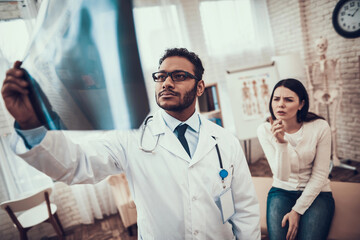 Indian doctor seeing patients in office. Doctor is looking at woman's x-ray.