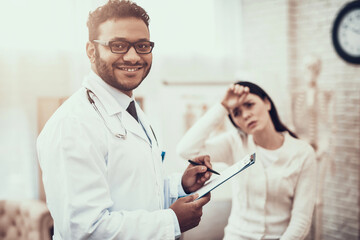 Indian doctor seeing patients in office. Doctor is listening to woman's symptoms. Woman has high...