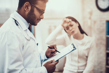 Indian doctor seeing patients in office. Doctor is listening to woman's symptoms. Woman has high...