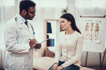 Indian doctor seeing patients in office. Doctor is listening to woman's symptoms.