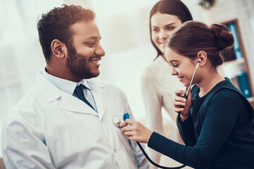 Indian doctor seeing patients in office. Daughter is using stethoscope on doctor.