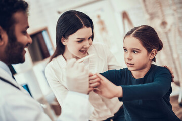Indian doctor seeing patients in office. Doctor is trying to examine girl's throat but daughter is...