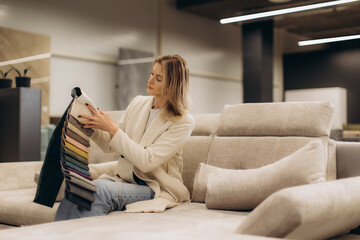 Woman Choosing Upholstery Fabric Samples While Sitting on a Modern Beige Sofa