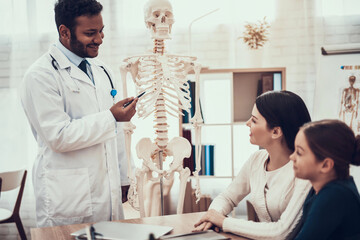 Indian doctor seeing patients in office. Doctor is showing skeleton to mother and daughter.