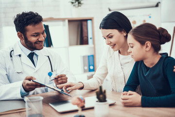 Indian doctor seeing patients in office. Doctor is taking notes listening to mother and daughter.