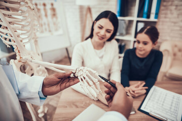 Indian doctor seeing patients in office. Doctor is showing skeleton to mother and daughter.