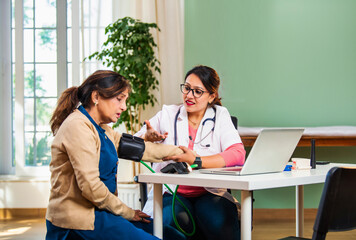 Young female doctor measuring blood pressure of elderly patient in clinic, discussing health issues