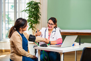 Young female doctor measuring blood pressure of elderly patient in clinic, discussing health issues