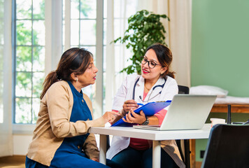 Indian Young female doctor discussing medical case report with senior patient in a lavish clinic