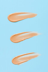 Makeup foundation texture swatch. BB cream, concealer, paint smear isolated on blue background. 