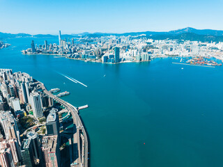 Aerial panorama showcases Hong Kong, China. Cityscape with skyscrapers and buildings stretches along the coast. Waterways and mountains visible in this wide scenic view. © YiuCheung