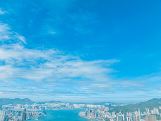 A stunning aerial panorama captures Hong Kong city under a vast blue sky with scattered clouds. The...