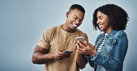 Happy couple, laughing or joke with phone in studio for social media or online network on a gray...