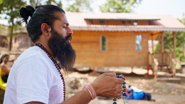 Rugged yogi meditates chanting with sacred beads outside