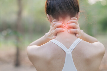 young Asian woman experiencing neck pain after exercise, holding her neck with both hands outdoors...
