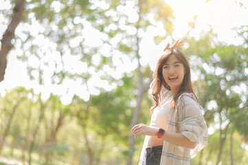 Asian woman enjoying summer outdoors, breathing fresh air with joyful smile in sunlit park...