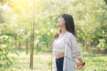 young woman enjoys sunlight in lush green park, wearing casual attire with relaxed and joyful expression