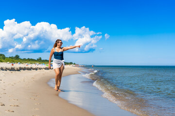 Summer vacation by sea. Beautiful middle aged woman walking along sea on sandy beach on sunny day....