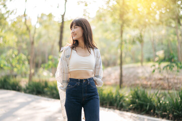 Asian woman enjoying summer outdoors, breathing fresh air in serene park, wearing casual attire...