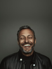 Obraz premium Middle-aged man with a confident smile, wearing a leather jacket, captured in a moody yet inviting studio portrait.