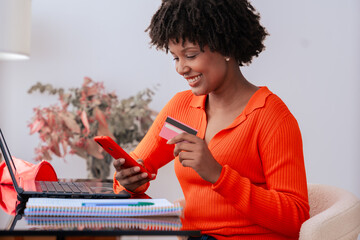 African american student making an online payment with a credit card while using a phone at home....