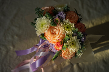 Peach roses, white chrysanthemums, and sprigs of evergreen create a beautiful bridal bouquet, tied...