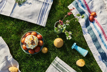 Traditional Easter picnic with homemade Easter cake and dyed eggs on a green lawn, decorated with...