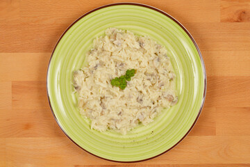 A top-down shot of a light-colored mushroom risotto served on a green plate, placed on a wooden surface