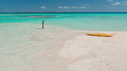 Woman standing on a beach next to yellow kayak. Travel summer background - small tropical island in turquoise water coral reef sea. Perfect sand beach drone flight