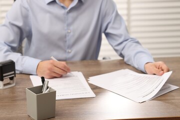 Man signing licensing agreement document at wooden table indoors, closeup