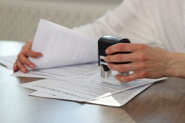 Fototapeta premium Woman stamping licensing agreement document at wooden table indoors, closeup