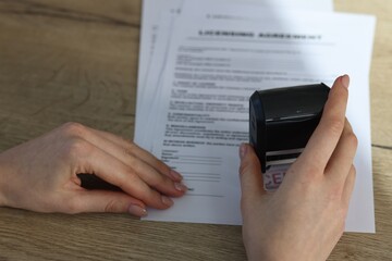 Woman stamping licensing agreement document at wooden table, closeup