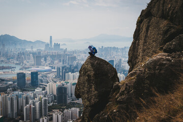 Woman traveller sit on the cliff edge enjoy the beautiful view of hong kong
