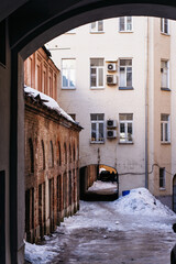A historic courtyard in winter, framed by an arched passageway. The contrast between the old brick...