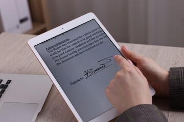 Fototapeta premium Electronic signature. Woman using tablet at wooden table, closeup