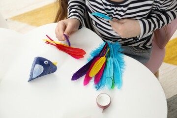 Little girl making paper bird at white table indoors, closeup. Child handmade craft