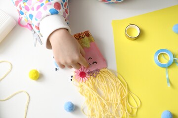 Little girl with handmade toy at white table, top view. Child creativity and craft