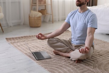 Man meditating near laptop on floor at home, closeup