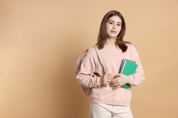Portrait of teenage girl with books and backpack on beige background. Space for text