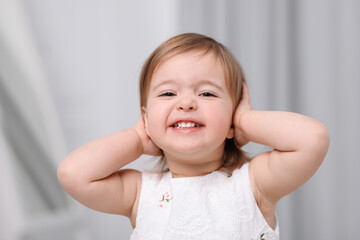 Cute little baby girl covering her ears on light grey background