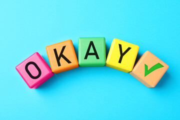 Colorful cubes with word Okay and check mark on light blue background, top view